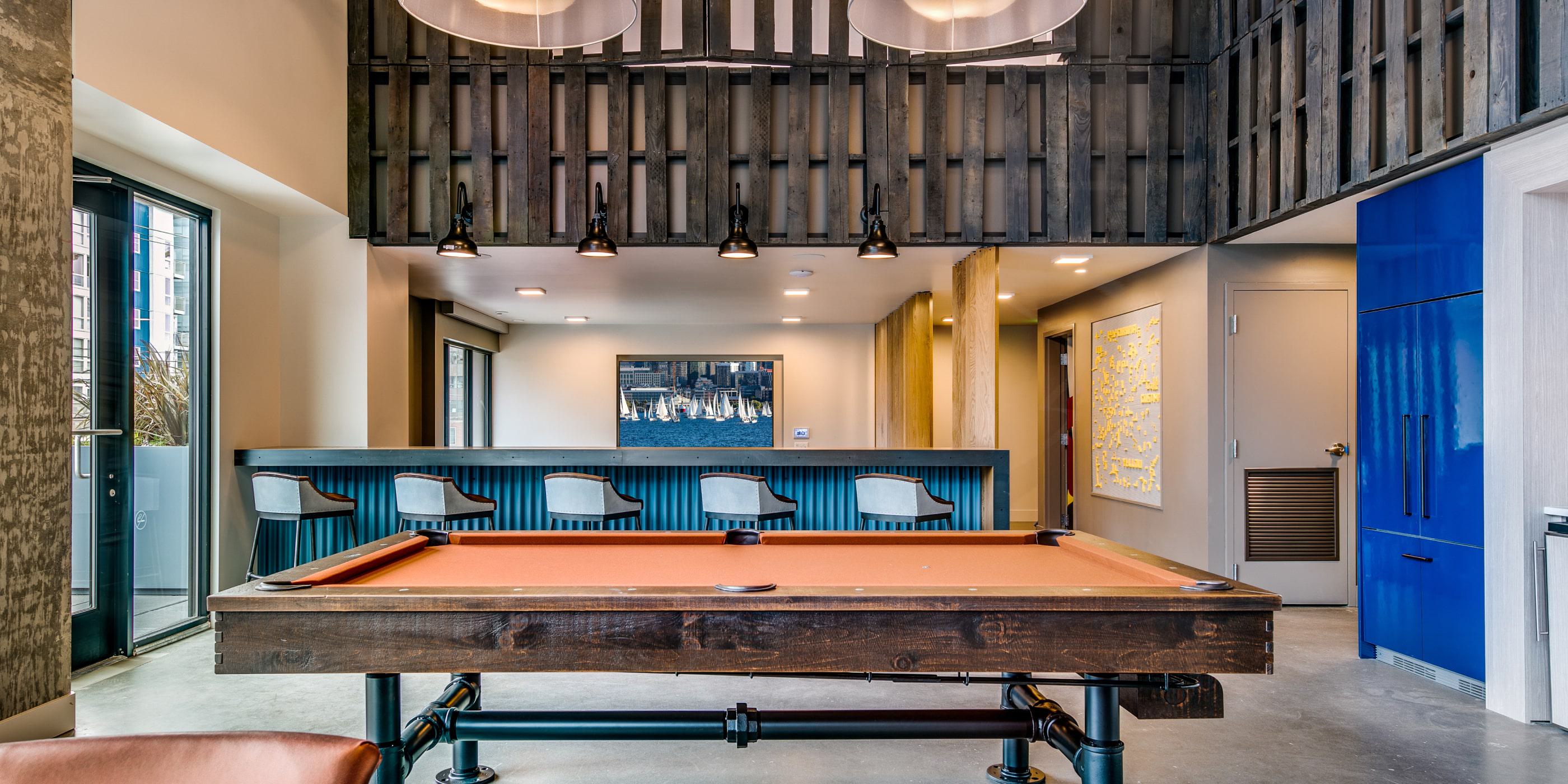 interior view of Chroma’s lounge featuring an orange-felt pool table, a bar with corrugated blue paneling and modern stools, wood accents, and large pendant lights under a high ceiling.
