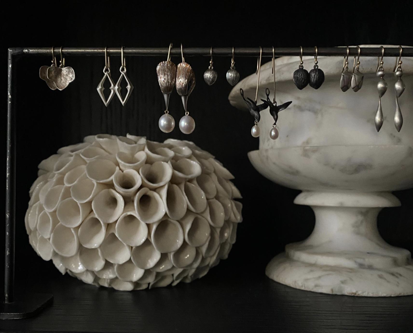 A display of delicate earrings at Métier boutique in San Francisco, featuring sculptural metalwork and pearls set against marble vessels.