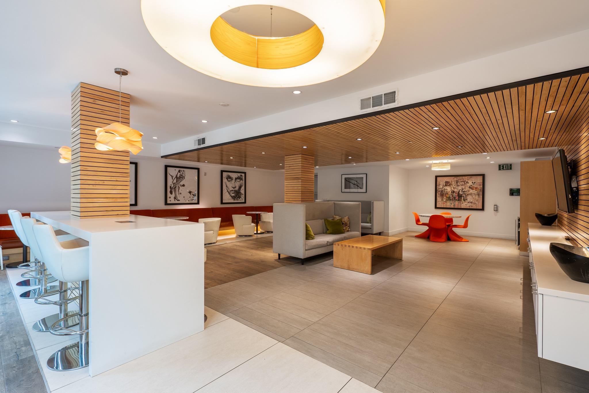 Coworking lounge at Alchemy with modern wood ceiling, bar seating, lounge chairs, and bold lighting fixtures.