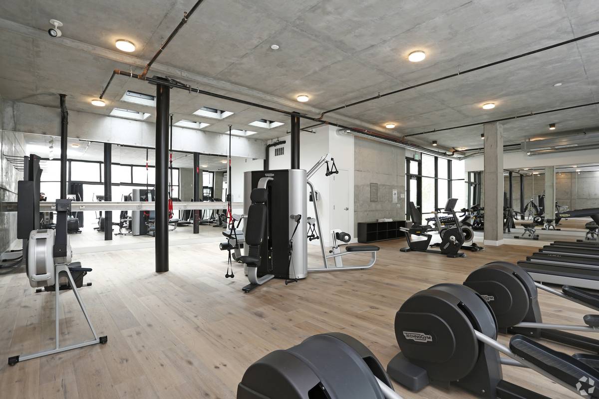 pacious fitness center at Alchemy with treadmills, strength machines, and open floors under exposed concrete ceilings and skylights.
