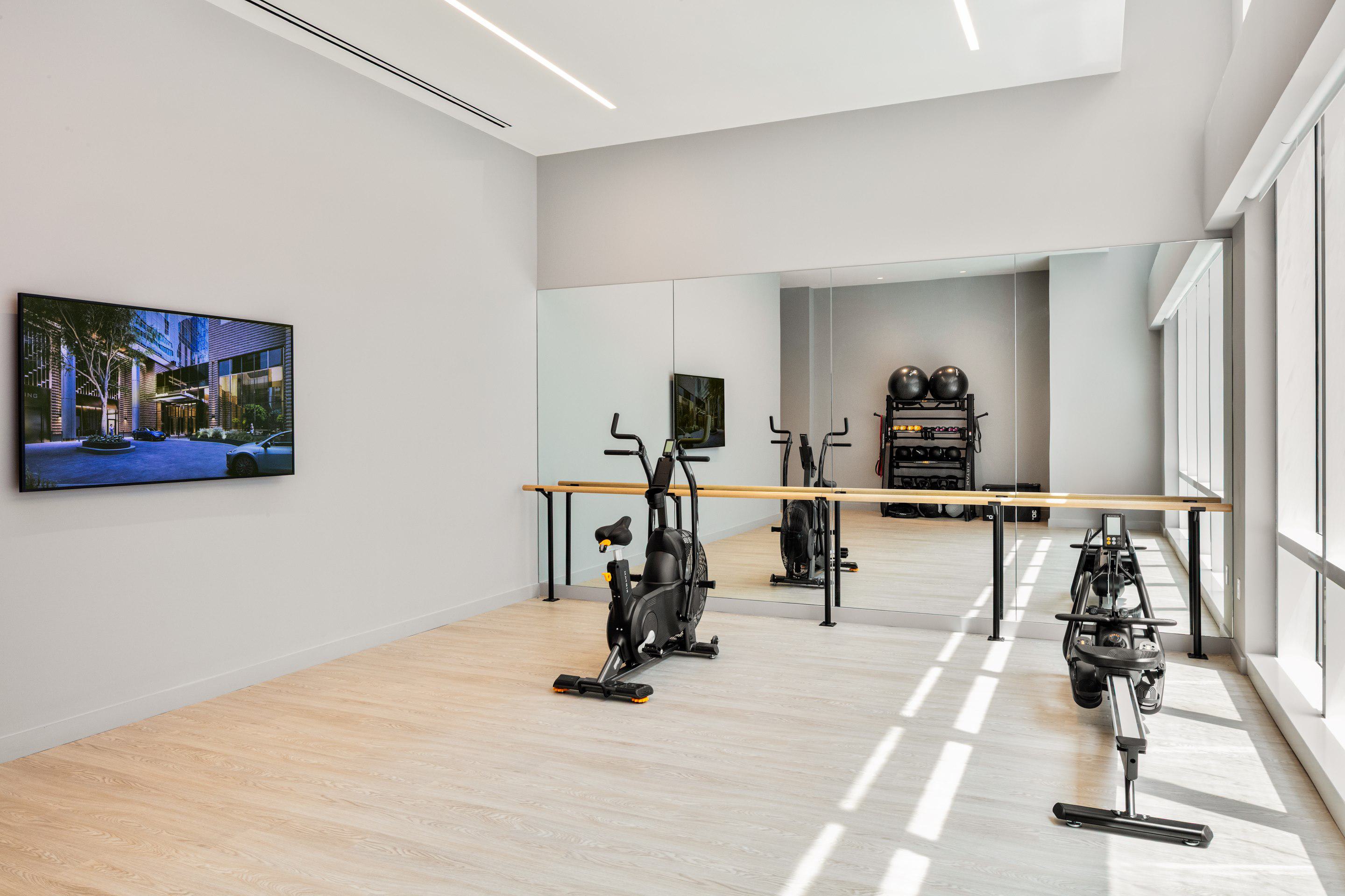 Bright spin studio with floor-to-ceiling windows, mirrored walls, spin bike, rowing machine, and training equipment in a sleek modern setting.