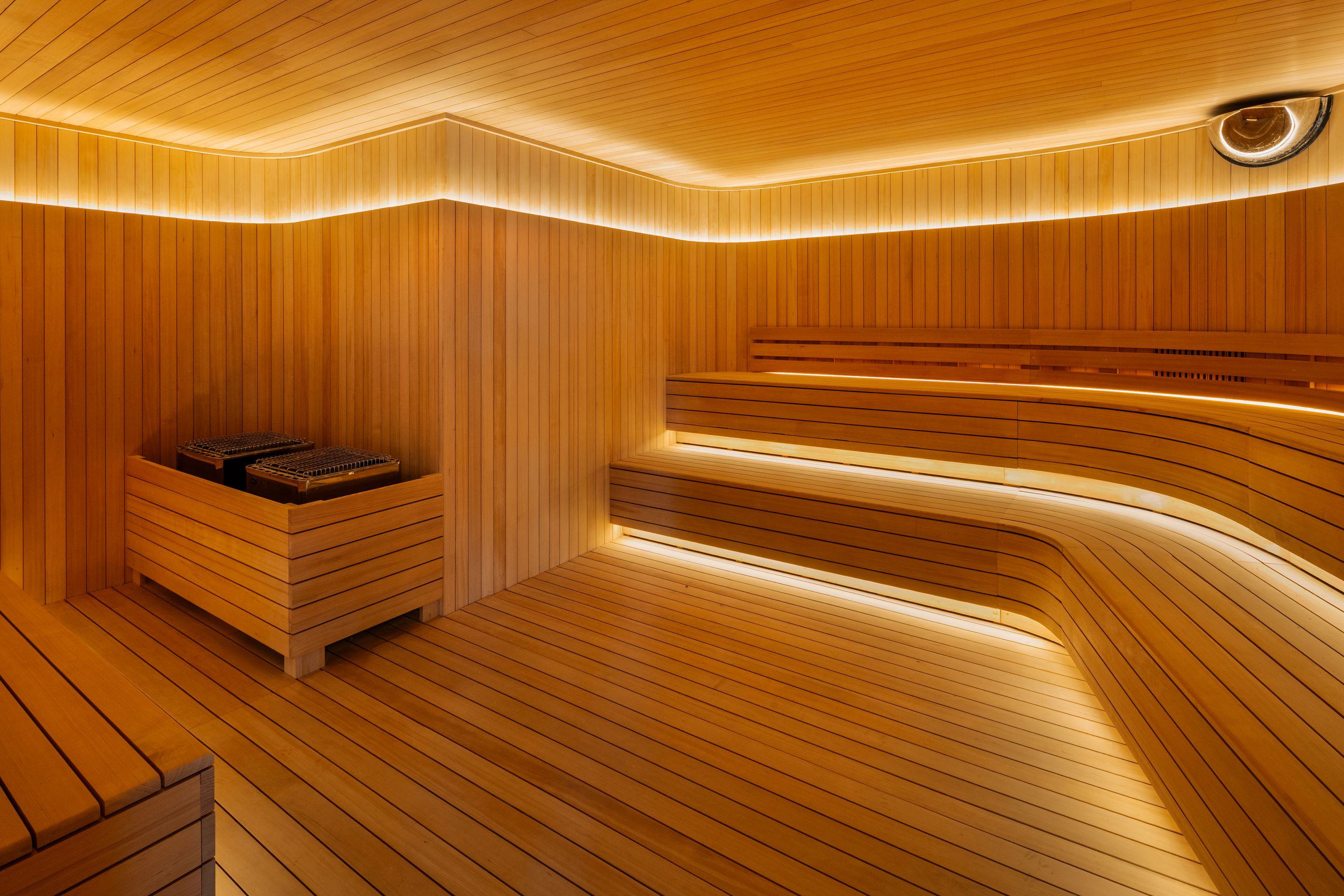 Spacious wood-lined sauna at Lumen with tiered bench seating and soft ambient lighting creating a warm, tranquil atmosphere.