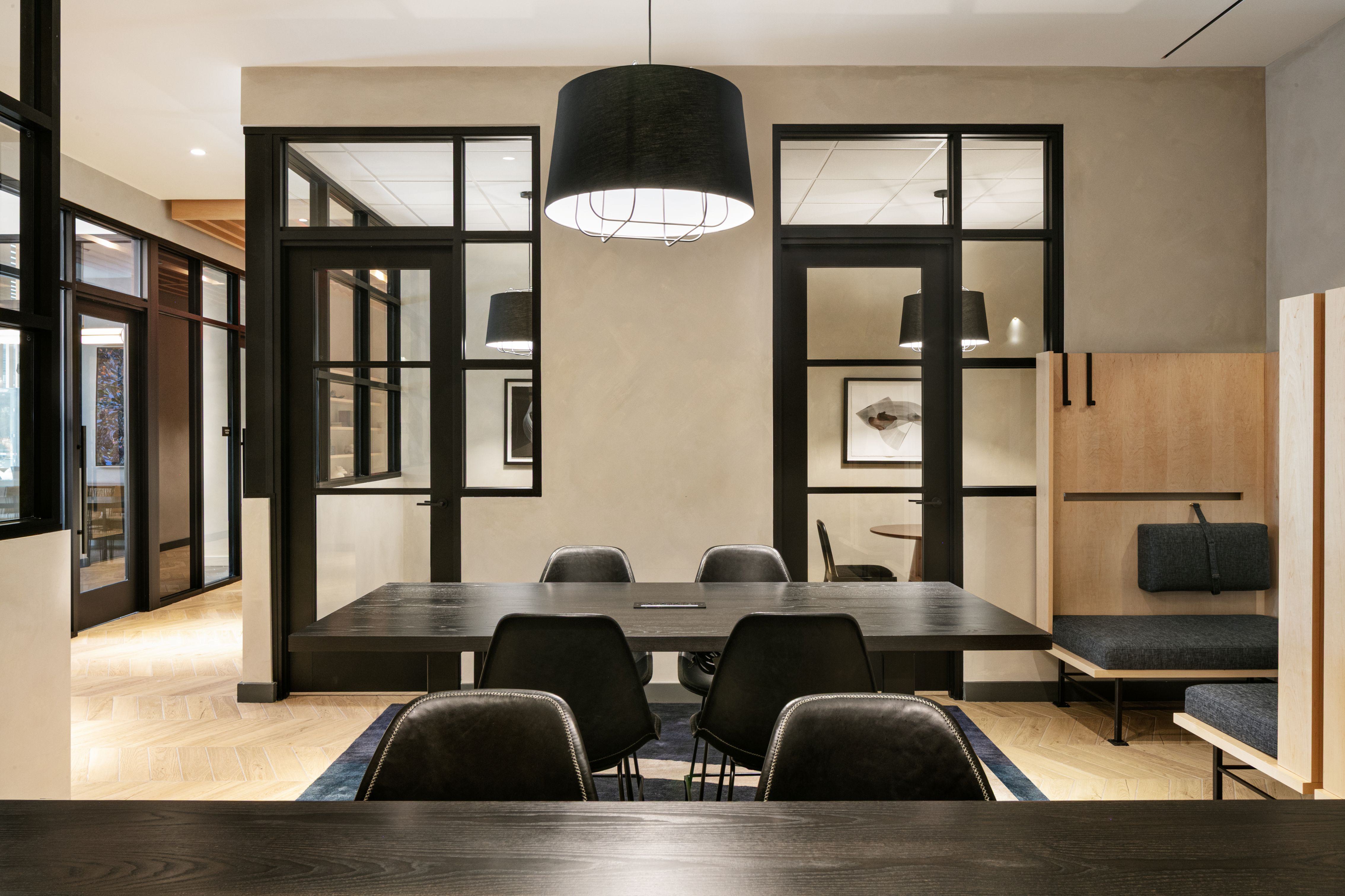 Loden coworking lounge with communal tables, black chairs, pendant lights, and semi-private wood-framed booths along the wall.