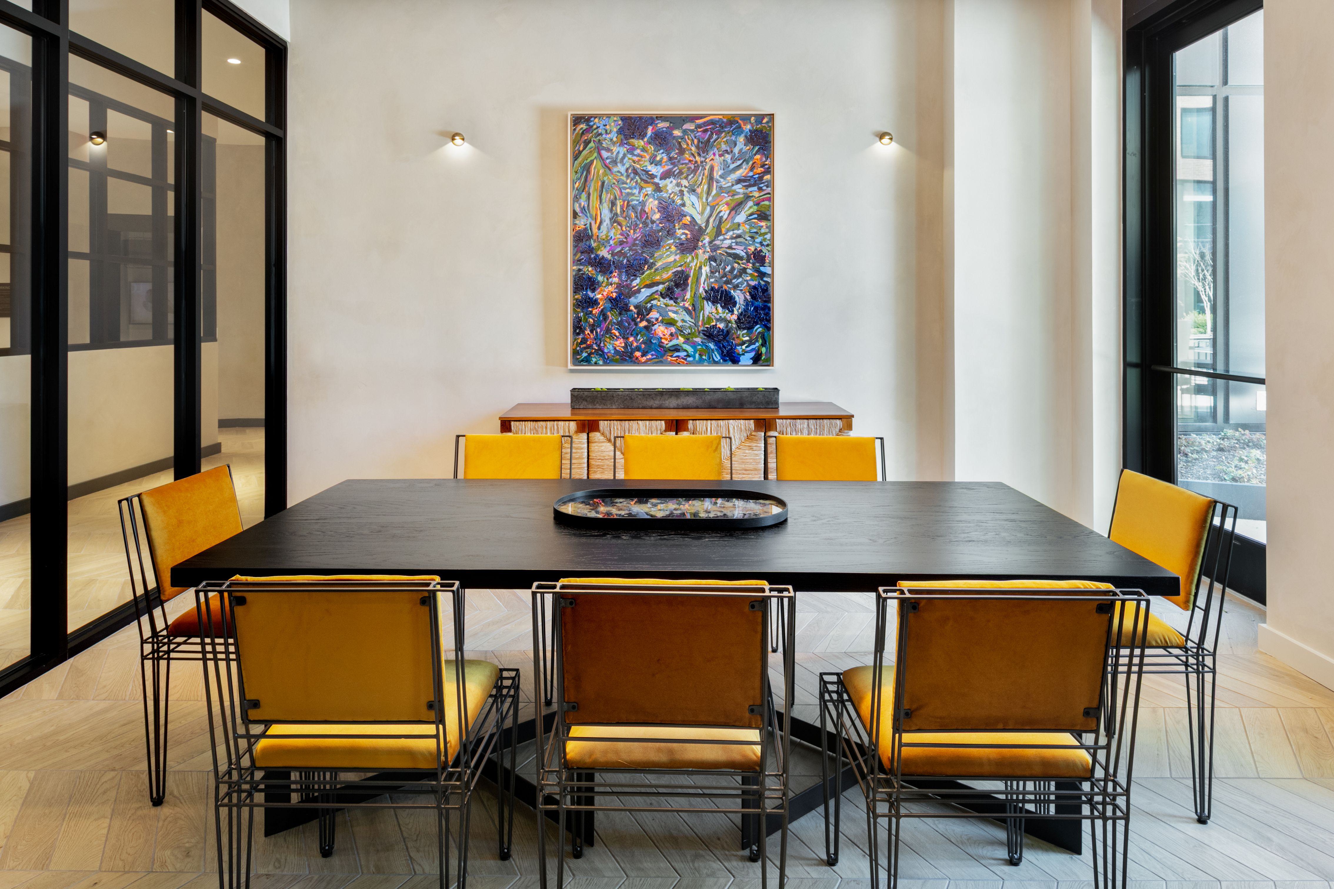 Conference room at Loden featuring a large black table with mustard-yellow chairs, colorful abstract artwork, and floor-to-ceiling glass walls.