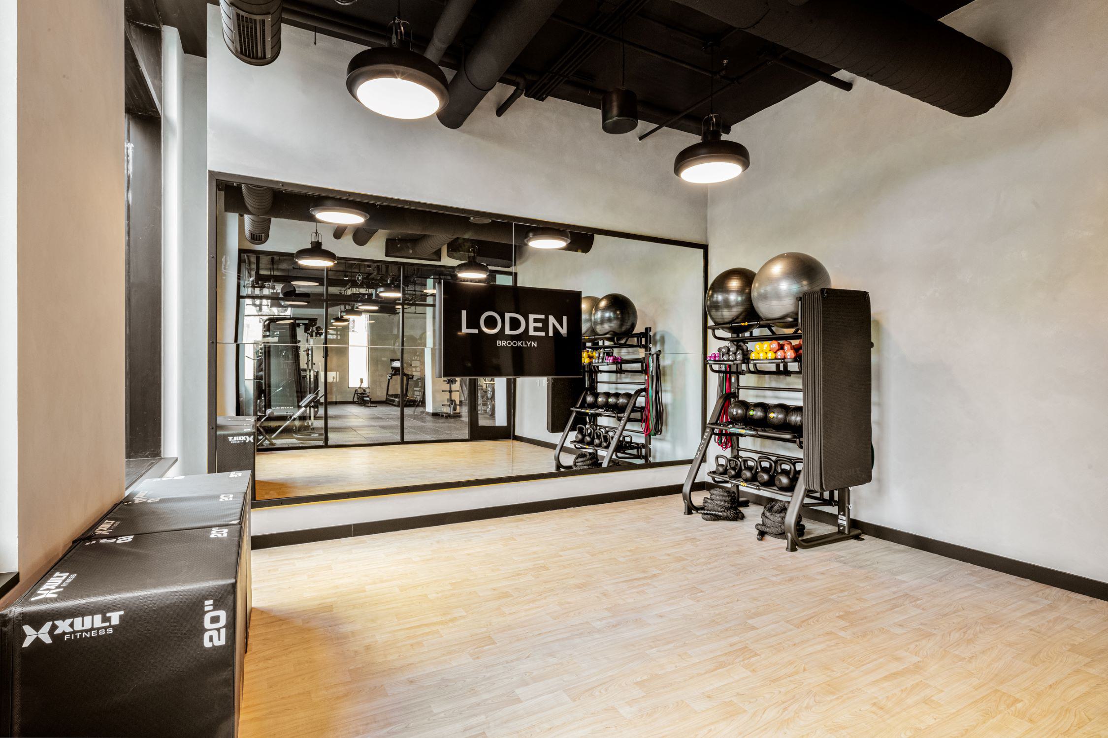 Loden yoga and fitness studio with mirrored wall, wood flooring, stability balls, kettlebells, resistance bands, and stacked mats.