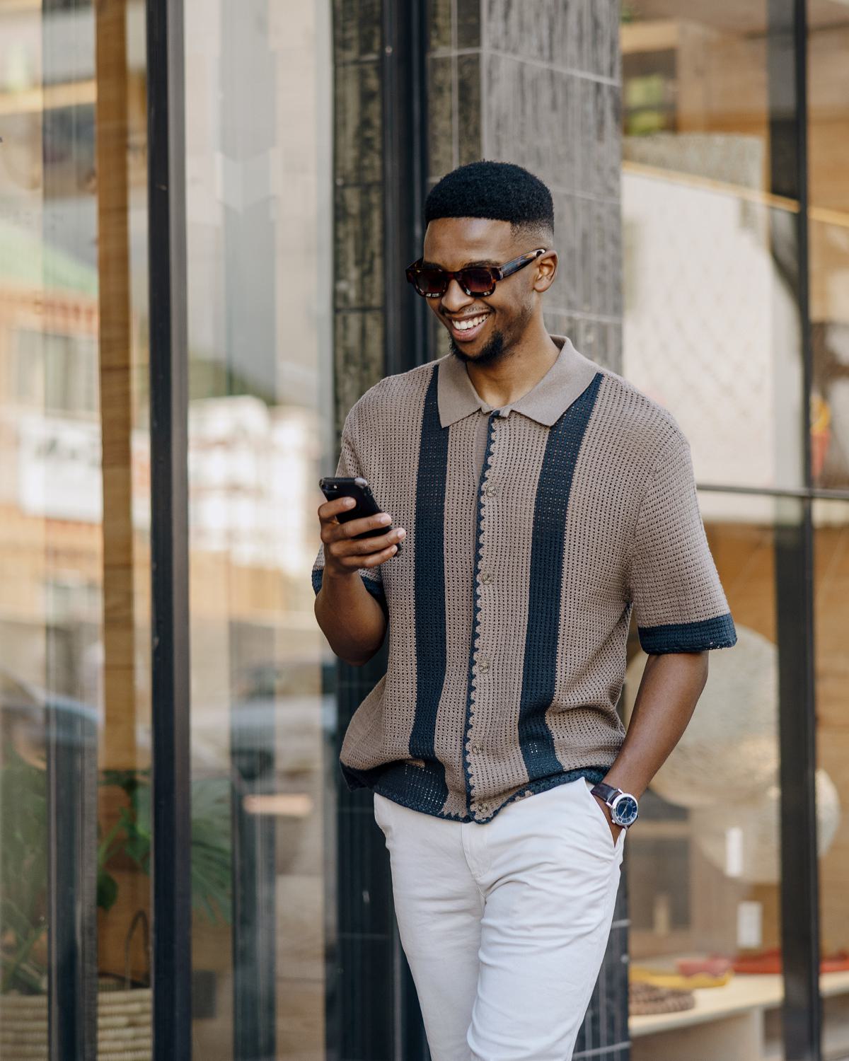 Stylish man walking through mid city, smiling while checking his phone.
