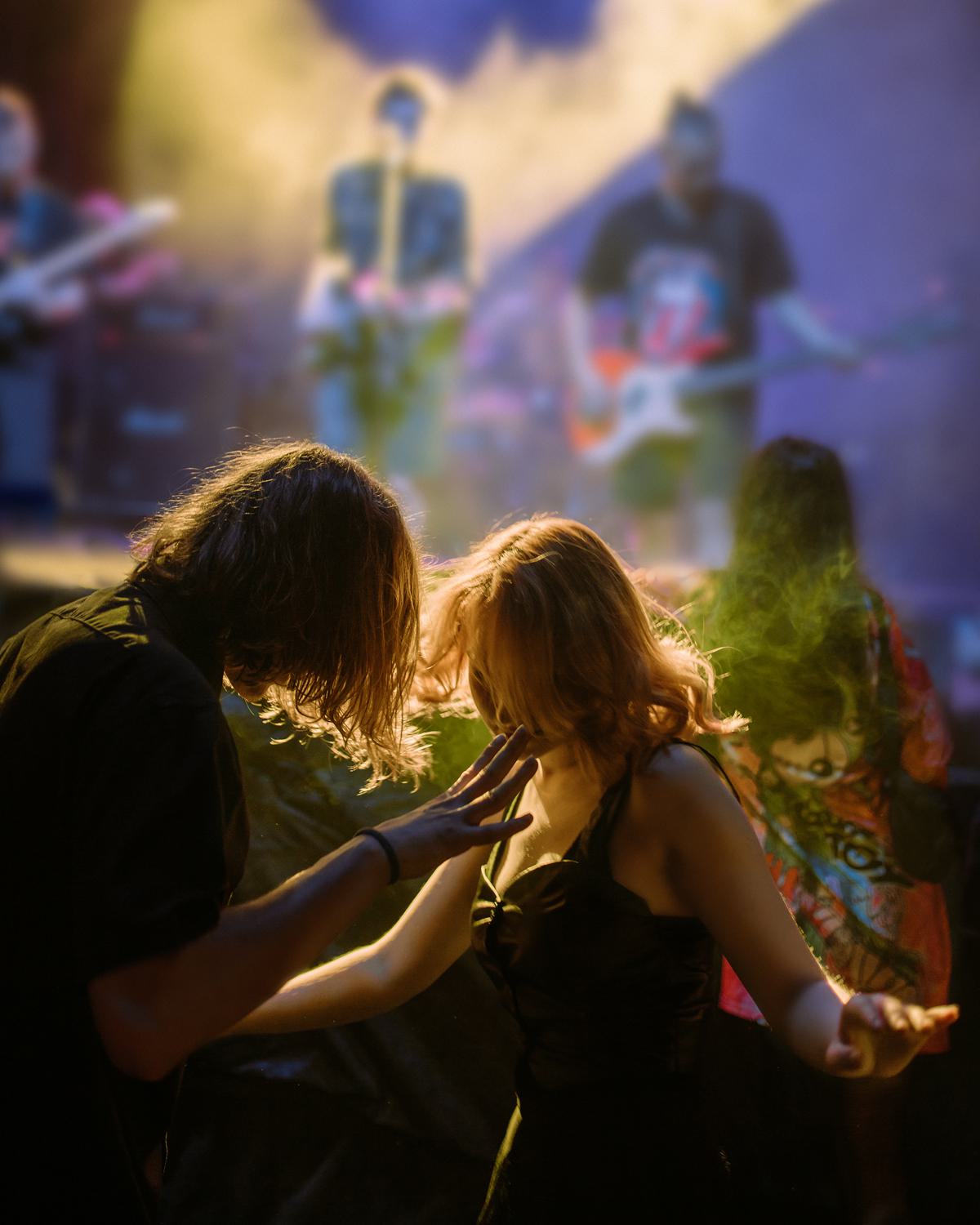 Couple dancing at a live concert under colorful stage lights.