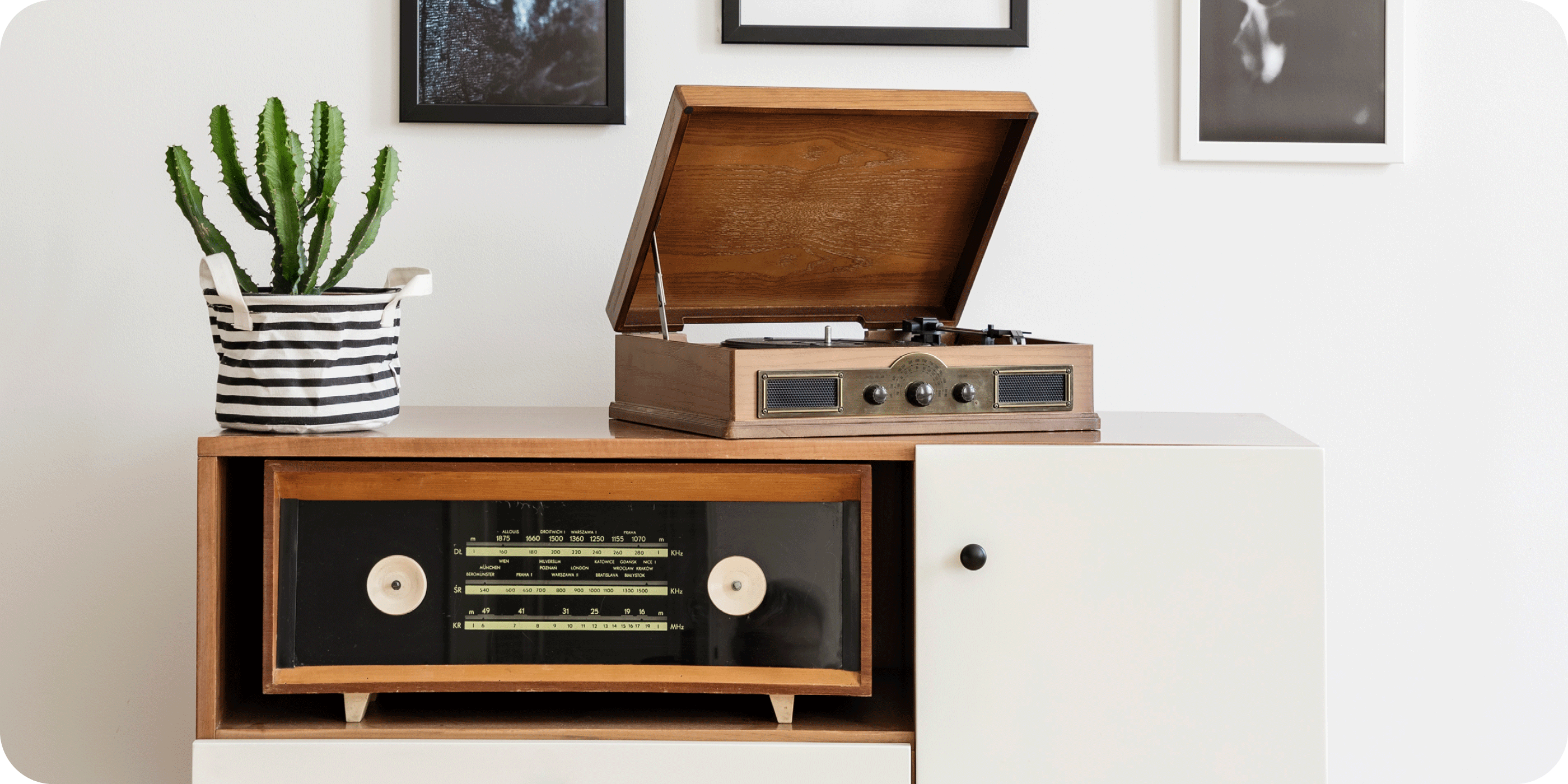 Mid-century cabinet with a vintage record player, striped planter, and framed wall art.