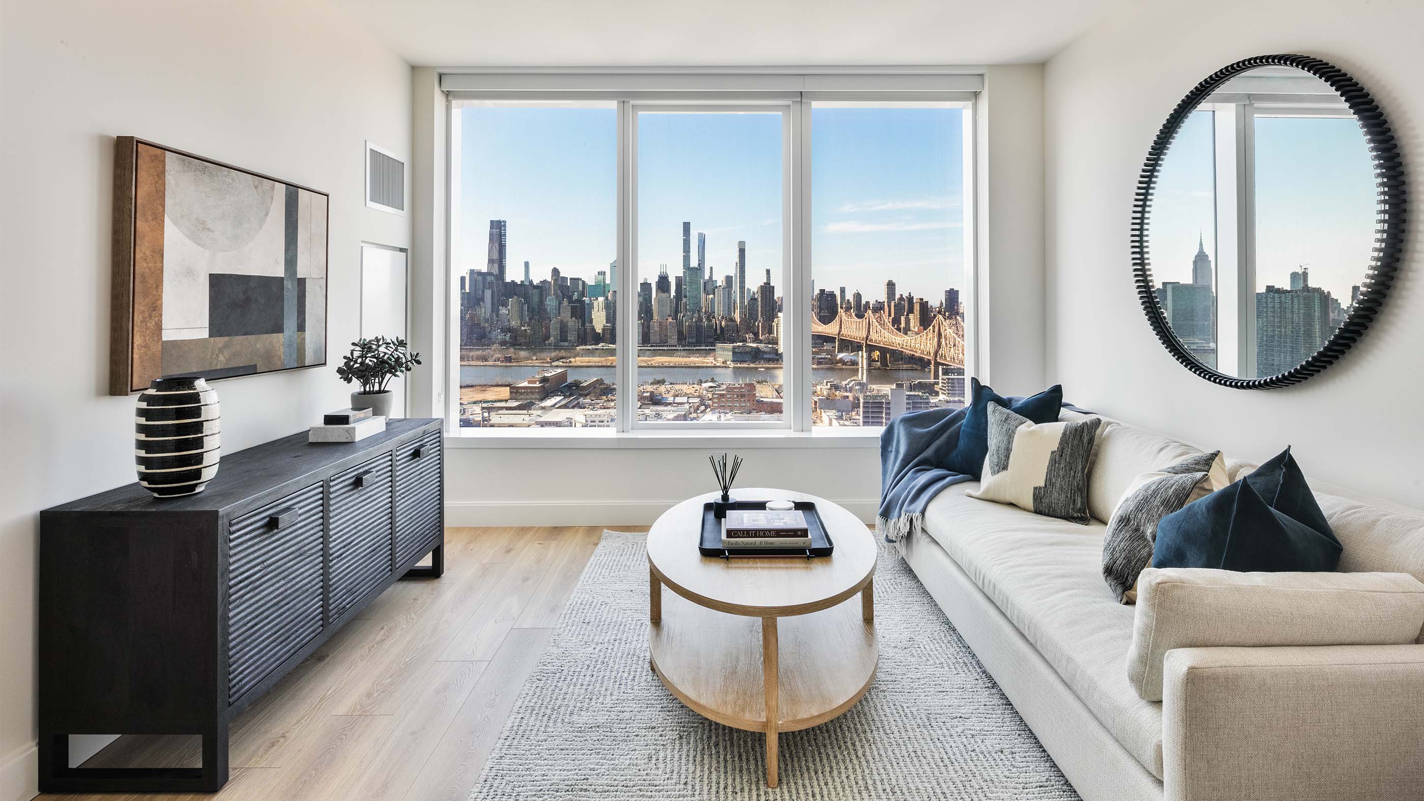 Modern Long Island City apartment living room with minimalist decor and floor-to-ceiling windows offering panoramic views of the Manhattan skyline and Queensboro Bridge.
