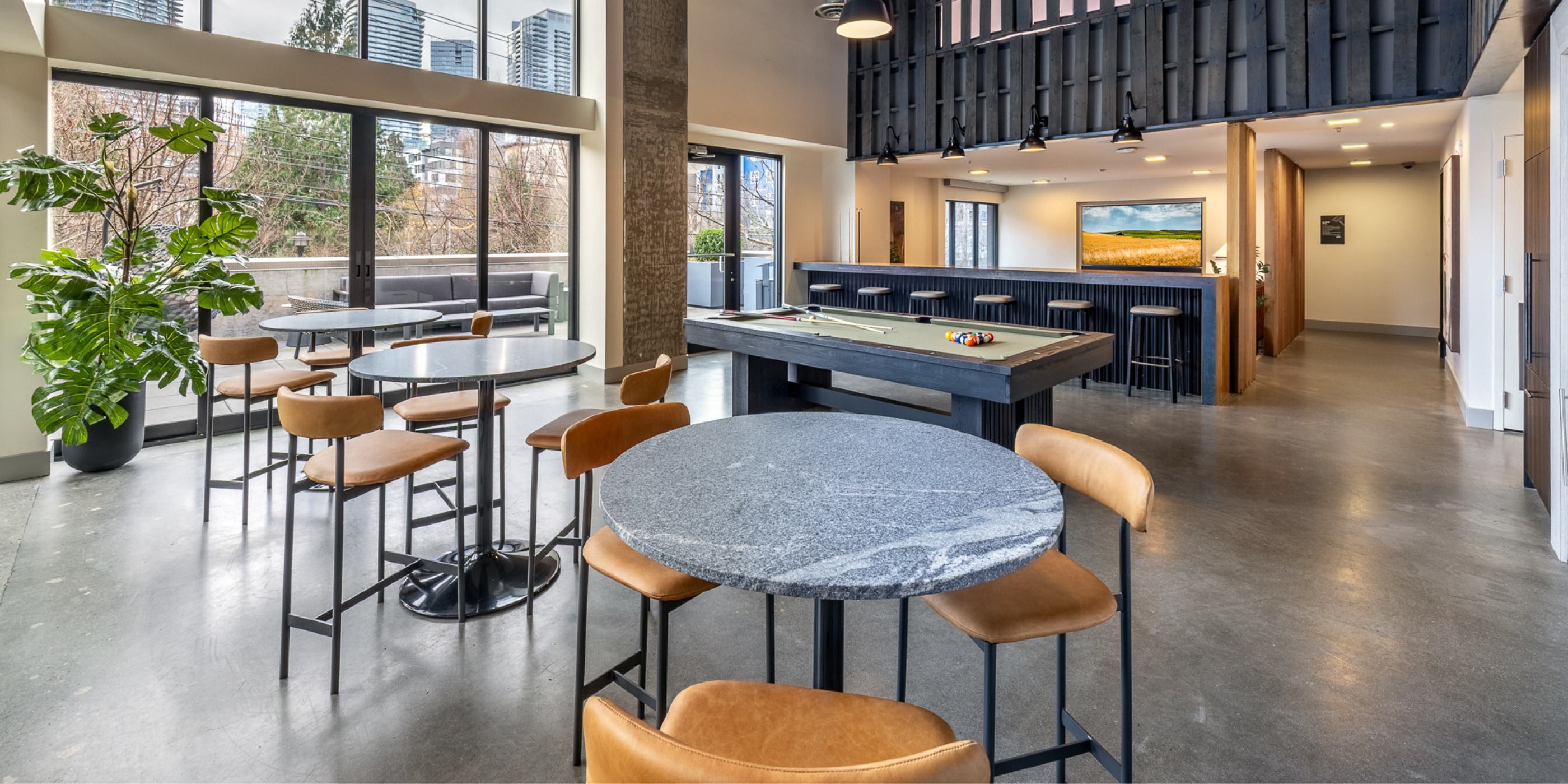 Rooftop lounge at Chroma SLU apartments with modern seating, large TV, and floor-to-ceiling windows opening to an outdoor terrace with city views.