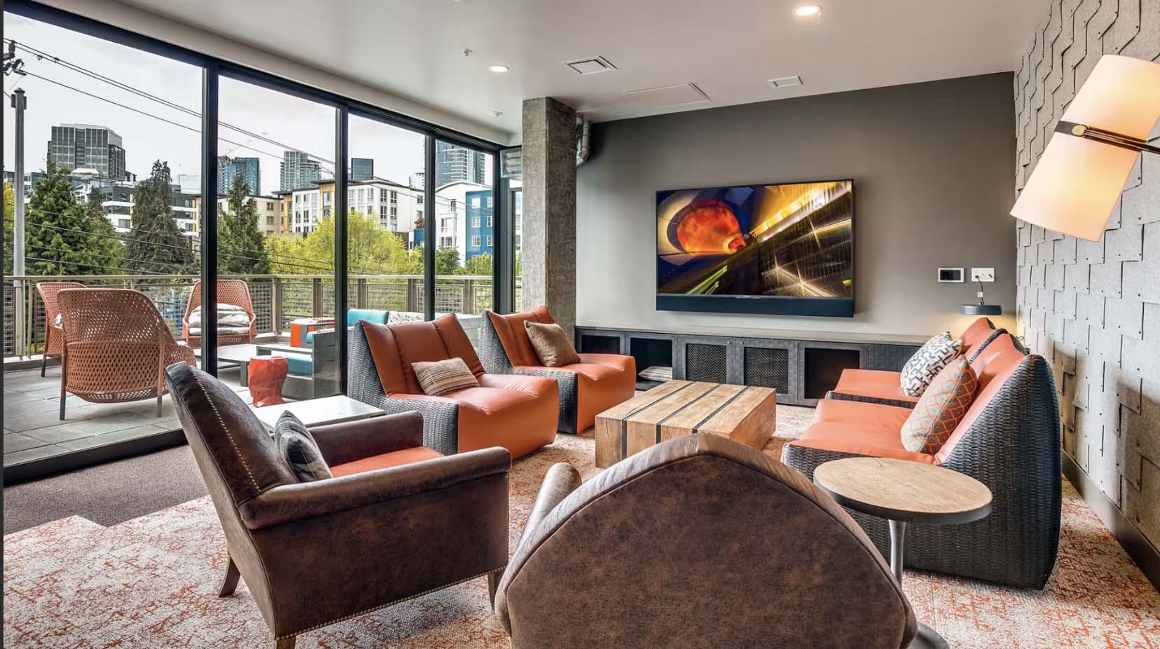 Rooftop lounge at Chroma SLU apartments with modern seating, large TV, and floor-to-ceiling windows opening to an outdoor terrace with city views.