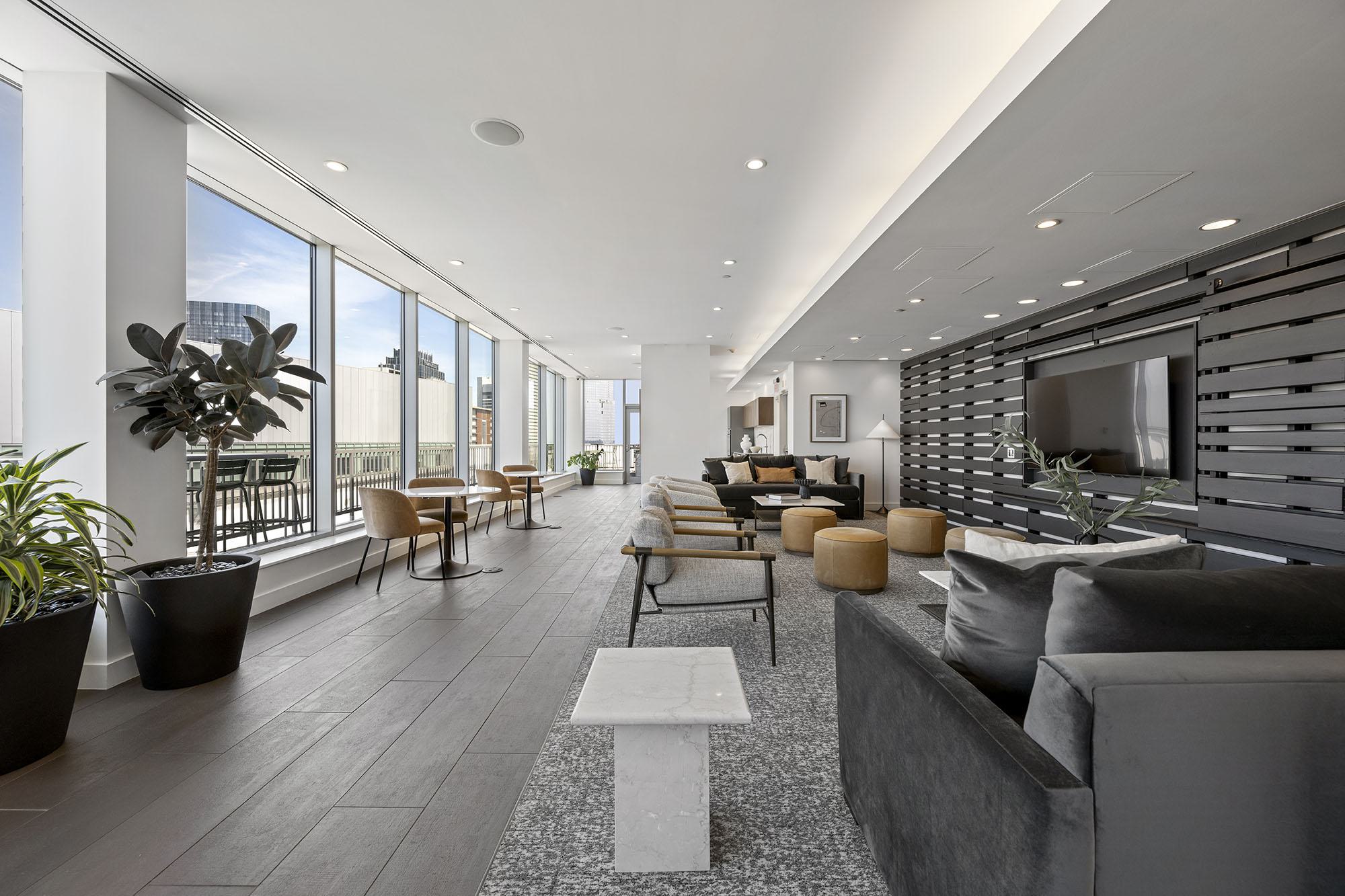 Elegant rooftop sky lounge at Luka on the Common featuring floor-to-ceiling windows, modern seating areas, and a TV wall with views of downtown Boston.