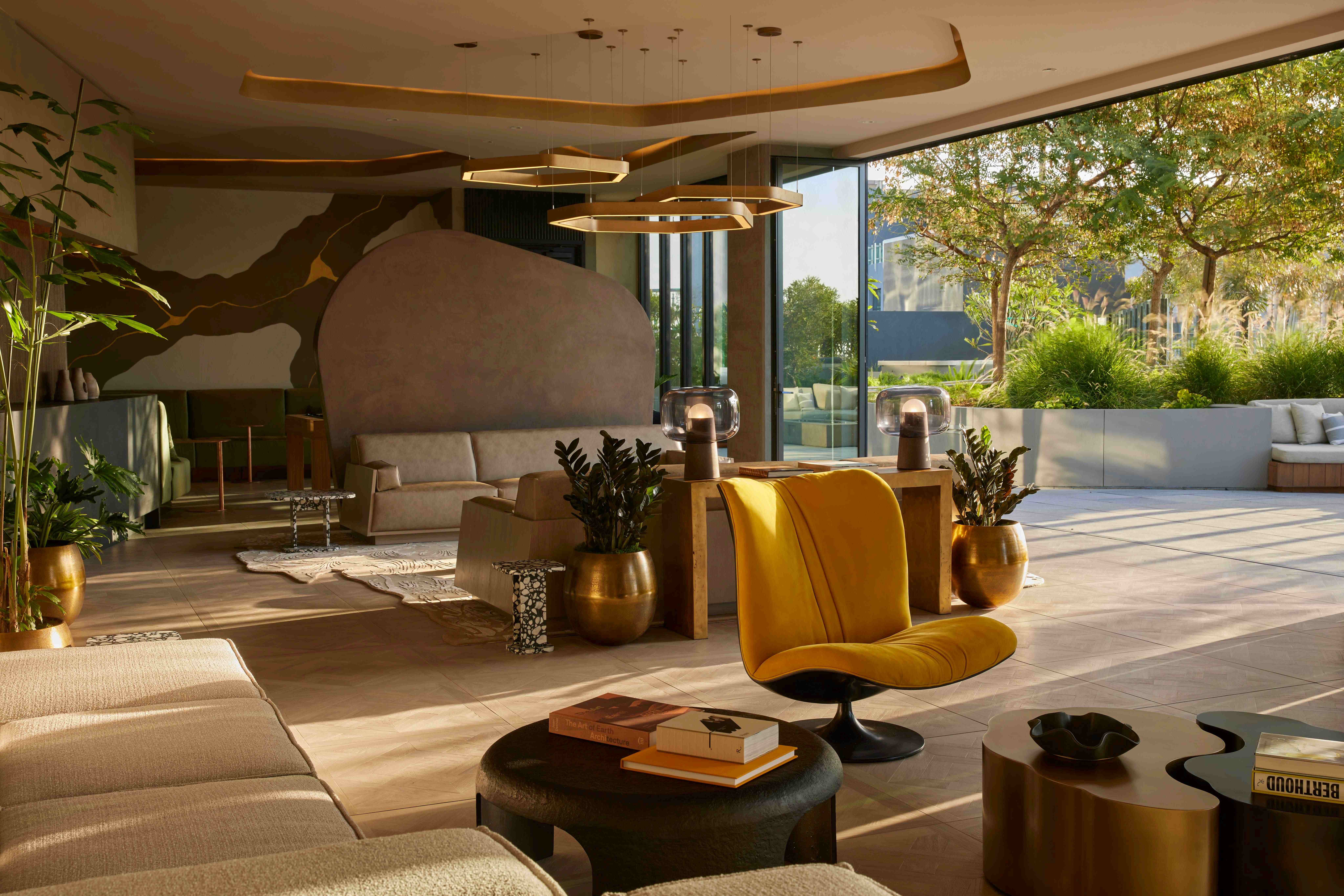 Lounge area at Alloy Apartments in Los Angeles featuring sculptural design, floor-to-ceiling windows, and an open connection to a landscaped terrace. Modern furniture, warm lighting, and natural textures create an inviting indoor-outdoor atmosphere.