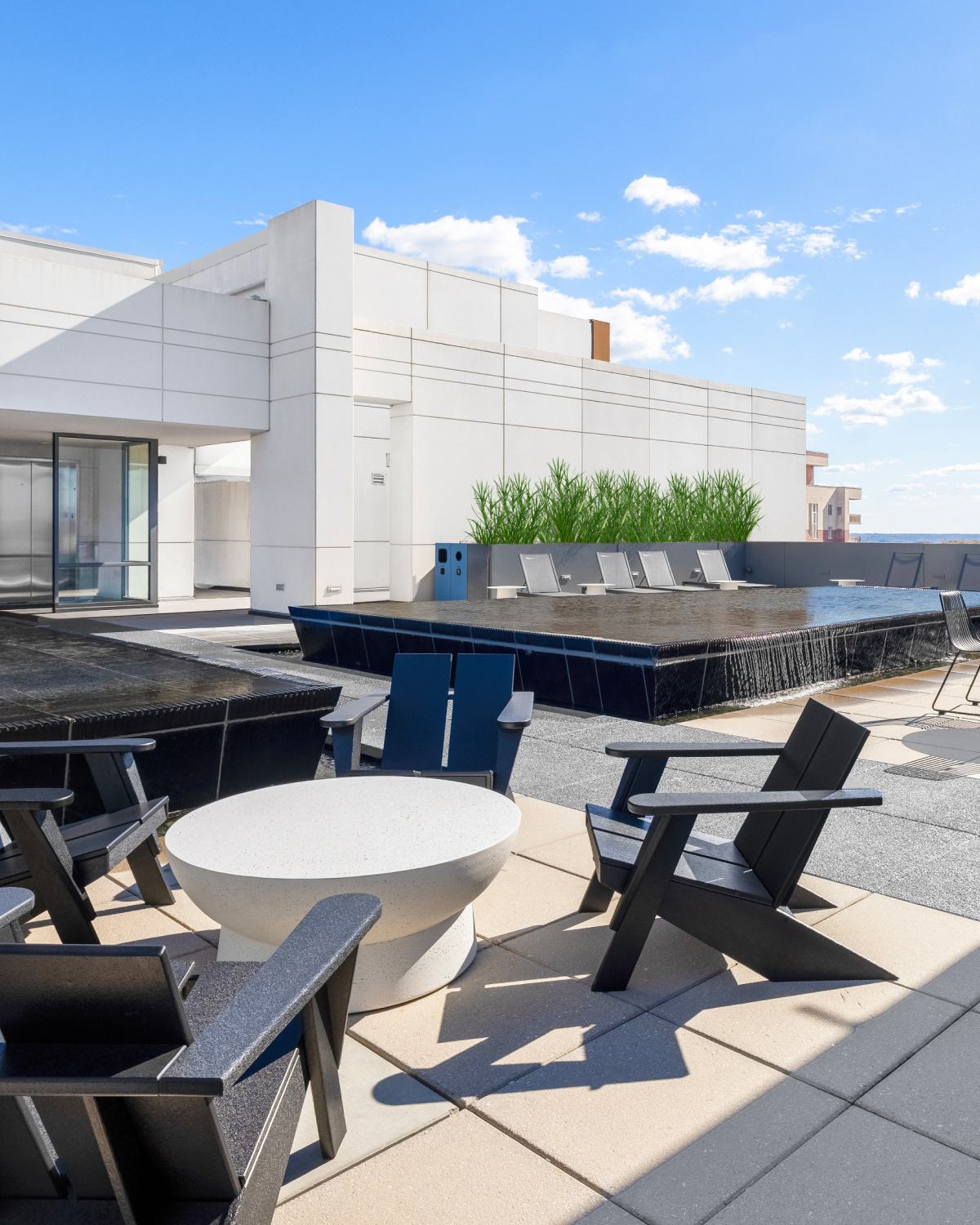 Rooftop terrace at Latitude Apartments in Virginia Square featuring a modern pool, outdoor lounge seating, dining areas, and open skyline views under a clear sky.