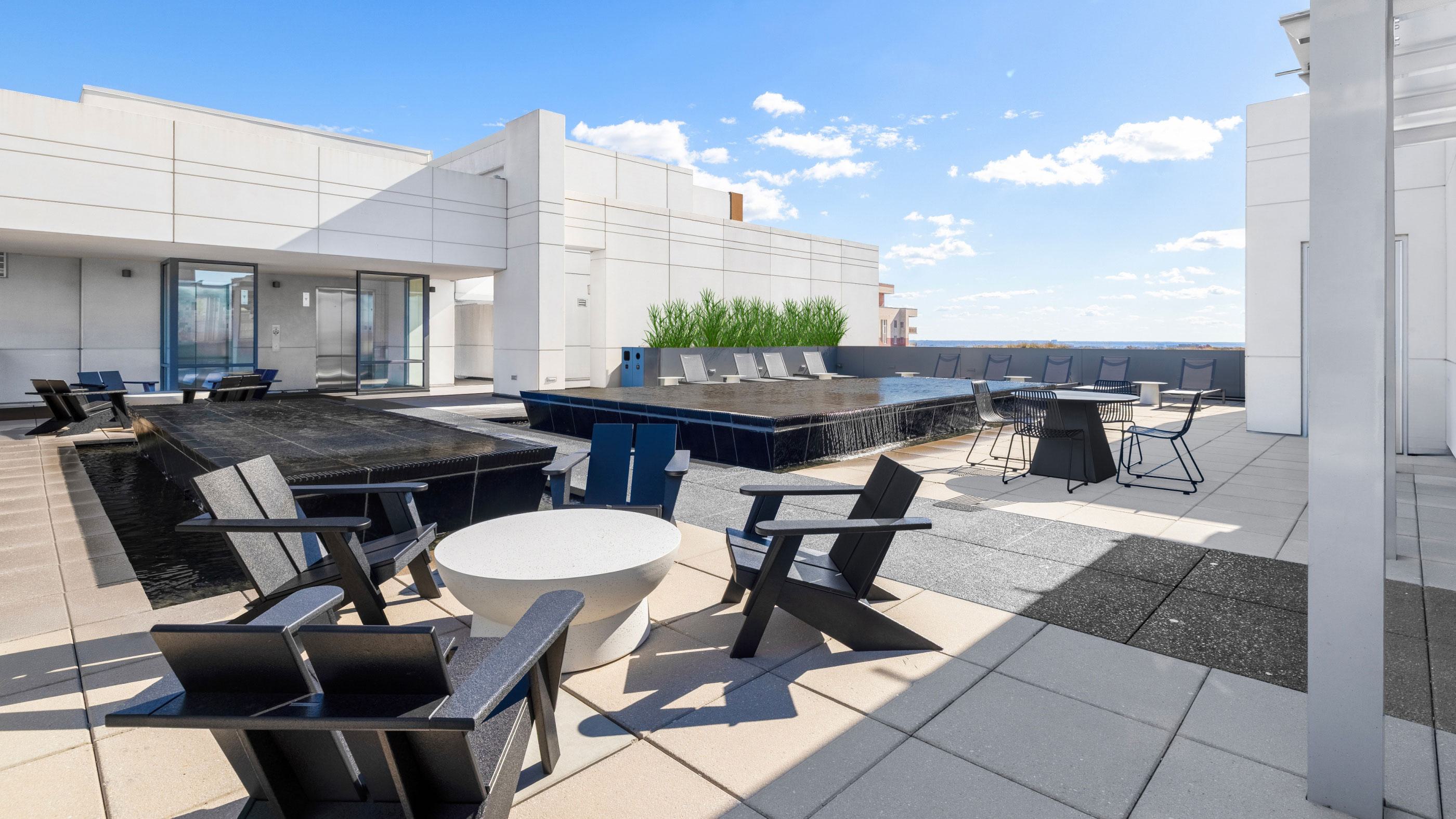 Rooftop terrace at Latitude Apartments in Virginia Square featuring a modern pool, outdoor lounge seating, dining areas, and open skyline views under a clear sky.