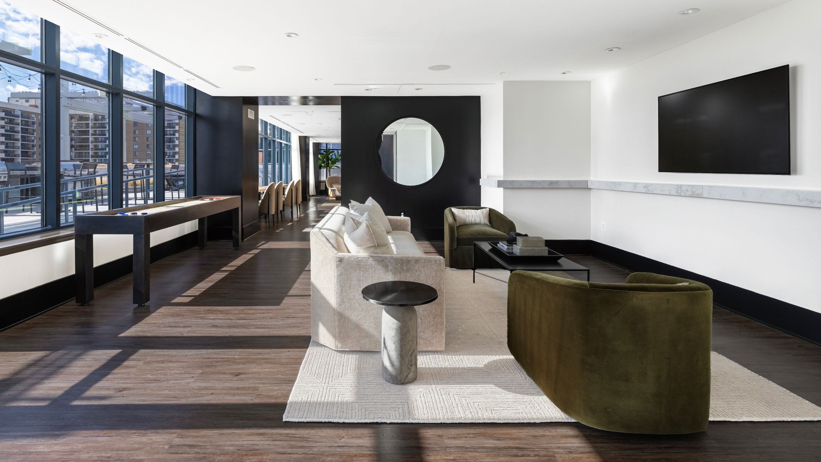 Resident lounge at Latitude Apartments in Virginia Square with contemporary seating, shuffleboard table, wall-mounted TV, and expansive windows providing natural light.