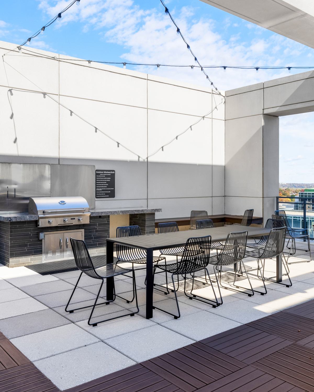 Outdoor dining terrace at Latitude Apartments in Virginia Square with a built-in grill, communal table seating, string lights, and elevated neighborhood views.