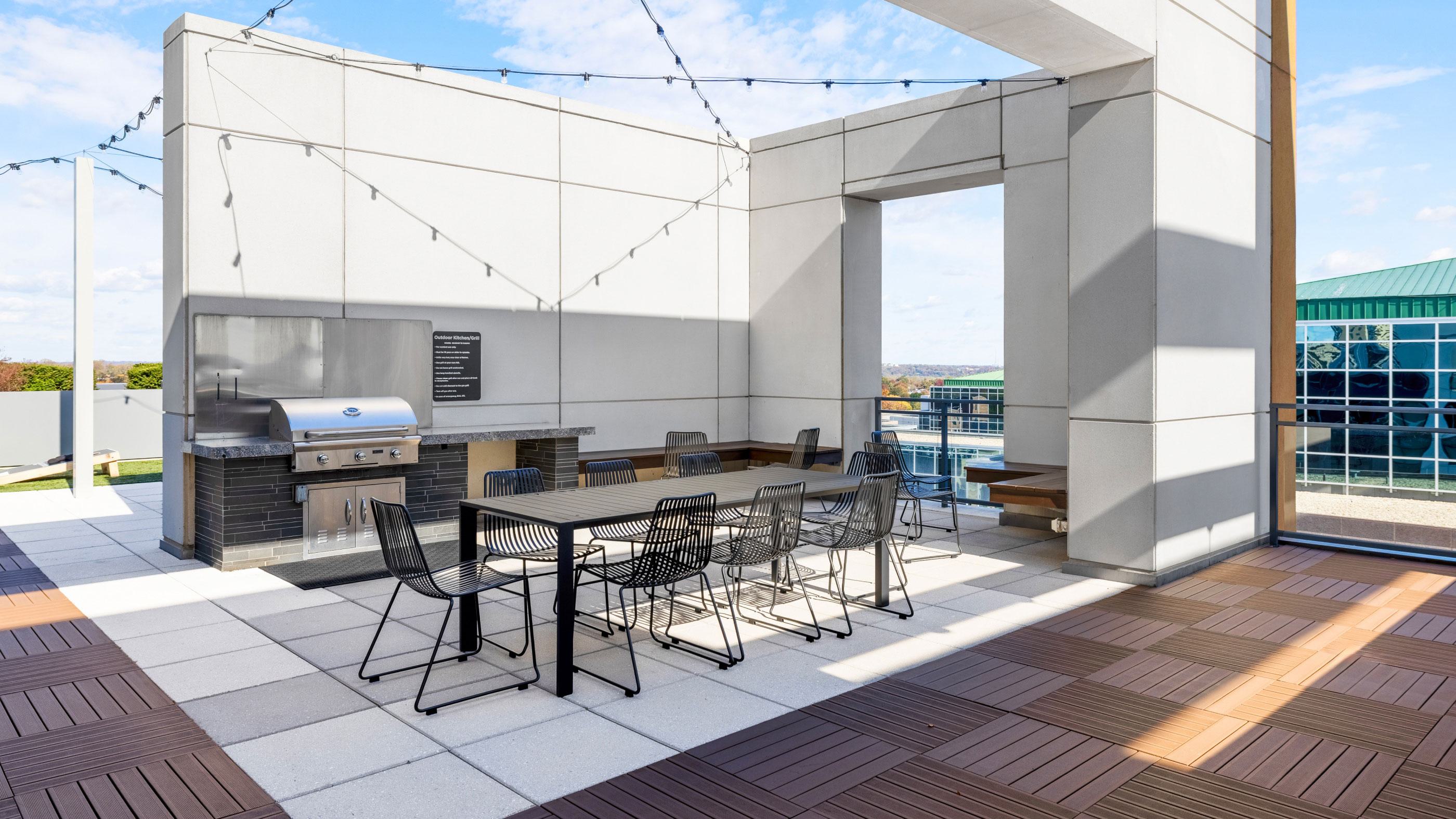 Outdoor dining terrace at Latitude Apartments in Virginia Square with a built-in grill, communal table seating, string lights, and elevated neighborhood views.