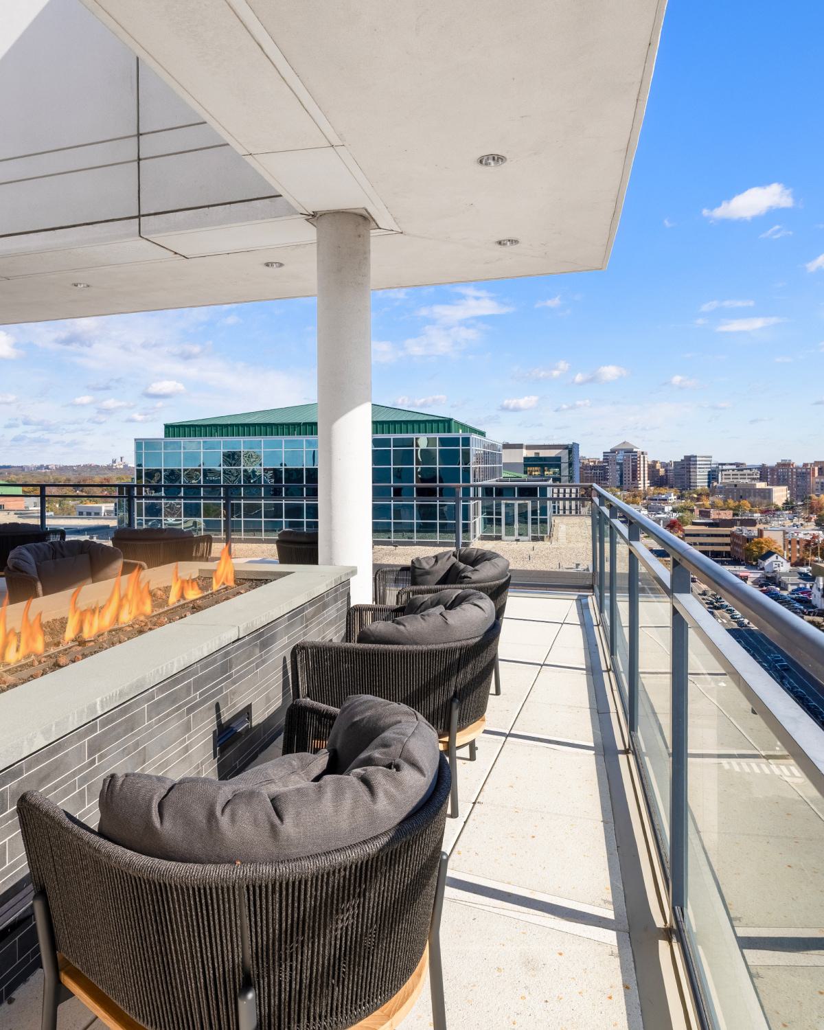 Rooftop terrace at Latitude Apartments in Virginia Square with a modern linear fire pit, cushioned lounge seating, glass railings, and expansive Arlington skyline views.