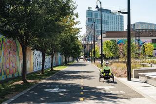 Cyclist riding along the Metropolitan Branch Trail in NoMa, Washington DC, surrounded by colorful murals, trees, and landscaped paths near Alethia Tanner Park, with modern apartments in the background.