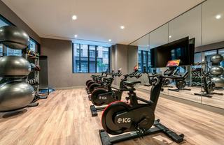 The Hale’s spin and yoga studio featuring a row of ICG stationary bikes facing mirrored walls and a large screen, with neatly organized stability balls, dumbbells, and medicine balls along the side wall on wood-look flooring in a bright, modern space.