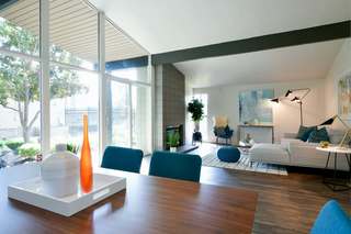 Bright mid-century–inspired living and dining area at The Arbors in Antelope, CA, featuring vaulted ceilings with exposed beams, floor-to-ceiling windows, and contemporary décor in shades of teal, gray, and white. Natural light fills the space, highlighting clean architectural lines and modern furnishings.