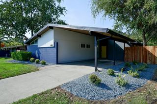 Mid-century modern single-family rental home at The Arbors in Antelope, CA, featuring an angular roofline with extended eaves forming a covered carport, geometric siding in white and navy, and minimalist landscaping with gravel beds and shrubs.