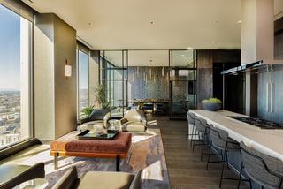 Private dining, kitchen, and lounge area at Atlas Oakland featuring floor-to-ceiling windows, geometric blue-and-gold wallpaper, marble island, and city views.