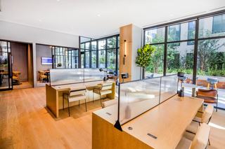 Bright coworking lounge at Atlas Oakland featuring floor-to-ceiling windows, built-in wood workstations with glass dividers, modern task lighting, and views of the outdoor terrace.