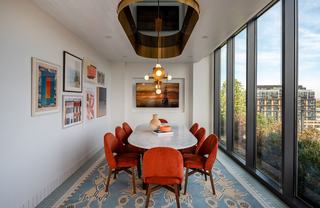 Private dining room at Theory featuring a marble oval table, rust velvet chairs, brass chandelier, and floor-to-ceiling windows with city views.