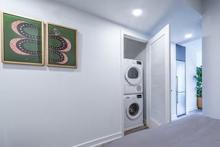 In-unit Bosch washer and dryer at Theory apartments, neatly stacked behind a louvered door in a bright modern hallway with framed wall art.