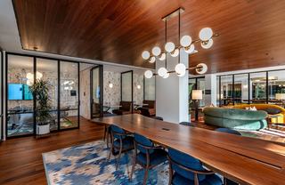 Coworking space at Theory featuring private work booths, a large communal table, lounge seating, a coffee bar, and a glass-walled conference room with bold wallpaper.