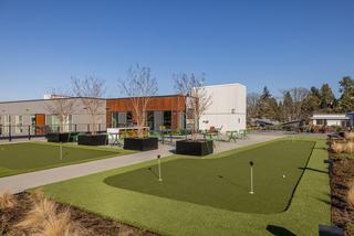 Rooftop putting green at Arlo Apartments featuring two turf greens with multiple holes, black planters, and green café seating overlooking the Columbia City neighborhood.