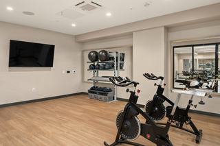 Bright spin and yoga studio at The Victor featuring two stationary bikes, wood floors, mirrored walls, a TV, and neatly organized workout gear.