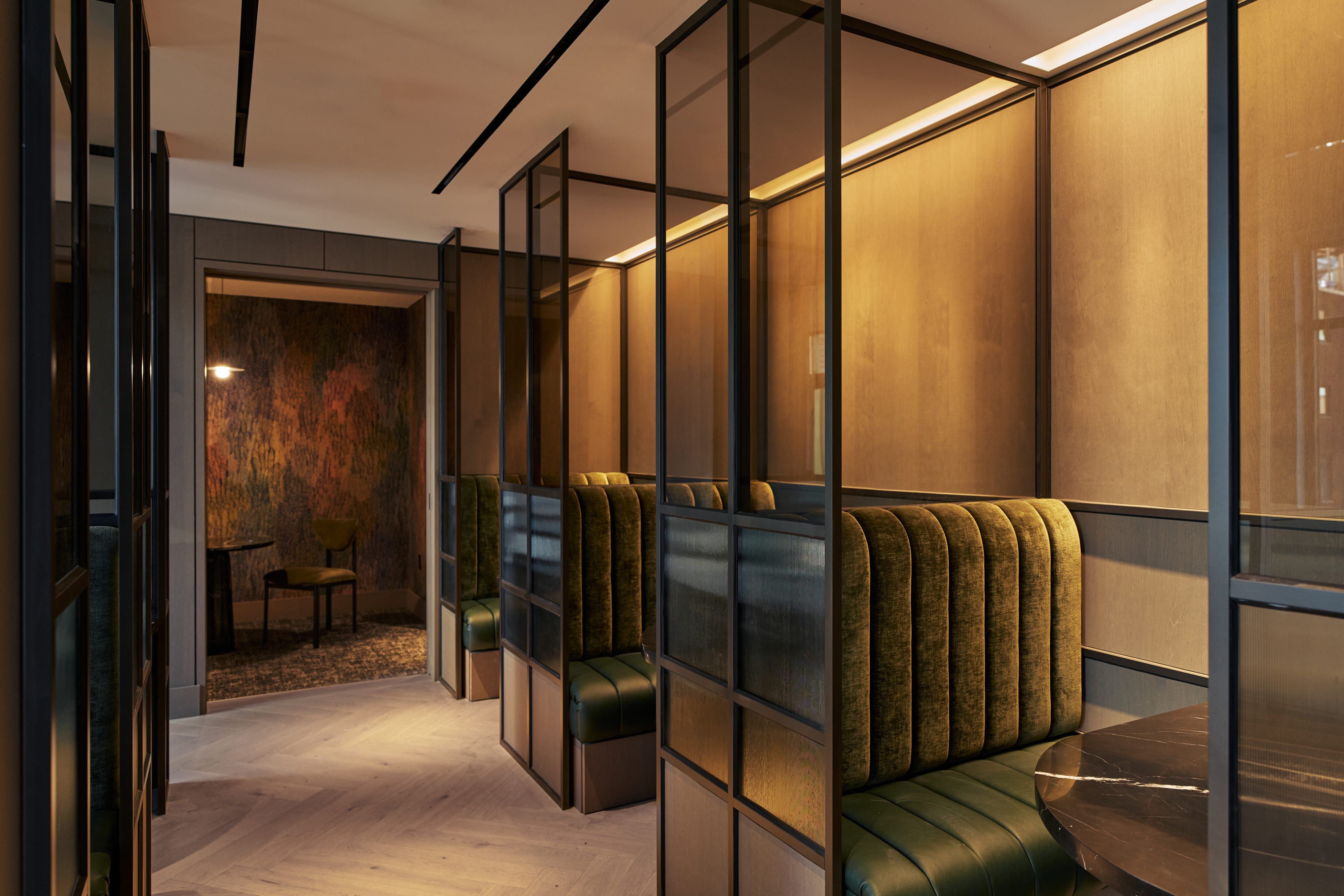 Row of semi-private coworking booths at Maison 78 featuring green channel-tufted seating, glass partitions, and warm wood paneling.