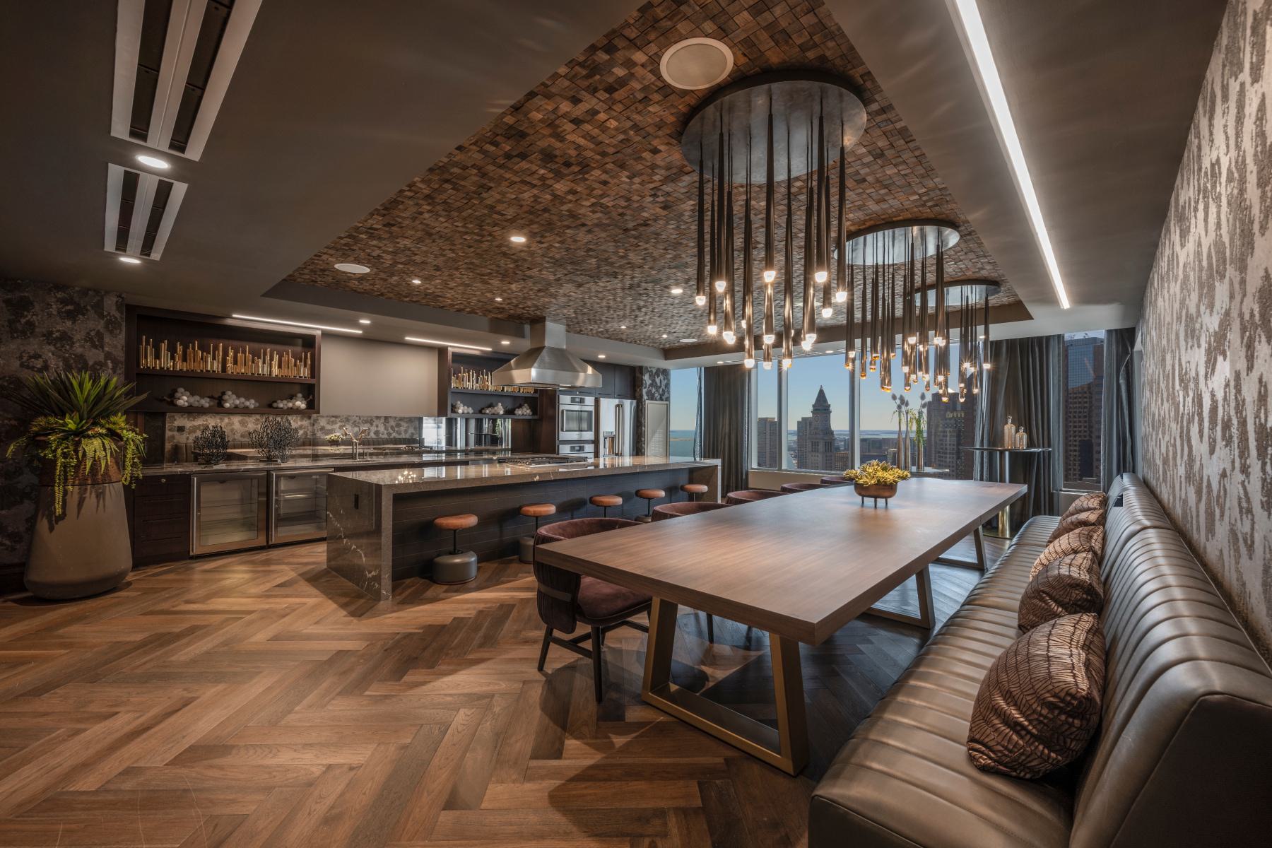 Luxury private dining room and chef’s kitchen at The Sudbury with a large stone island, wood dining table, pendant lighting, and floor-to-ceiling Boston skyline views.
