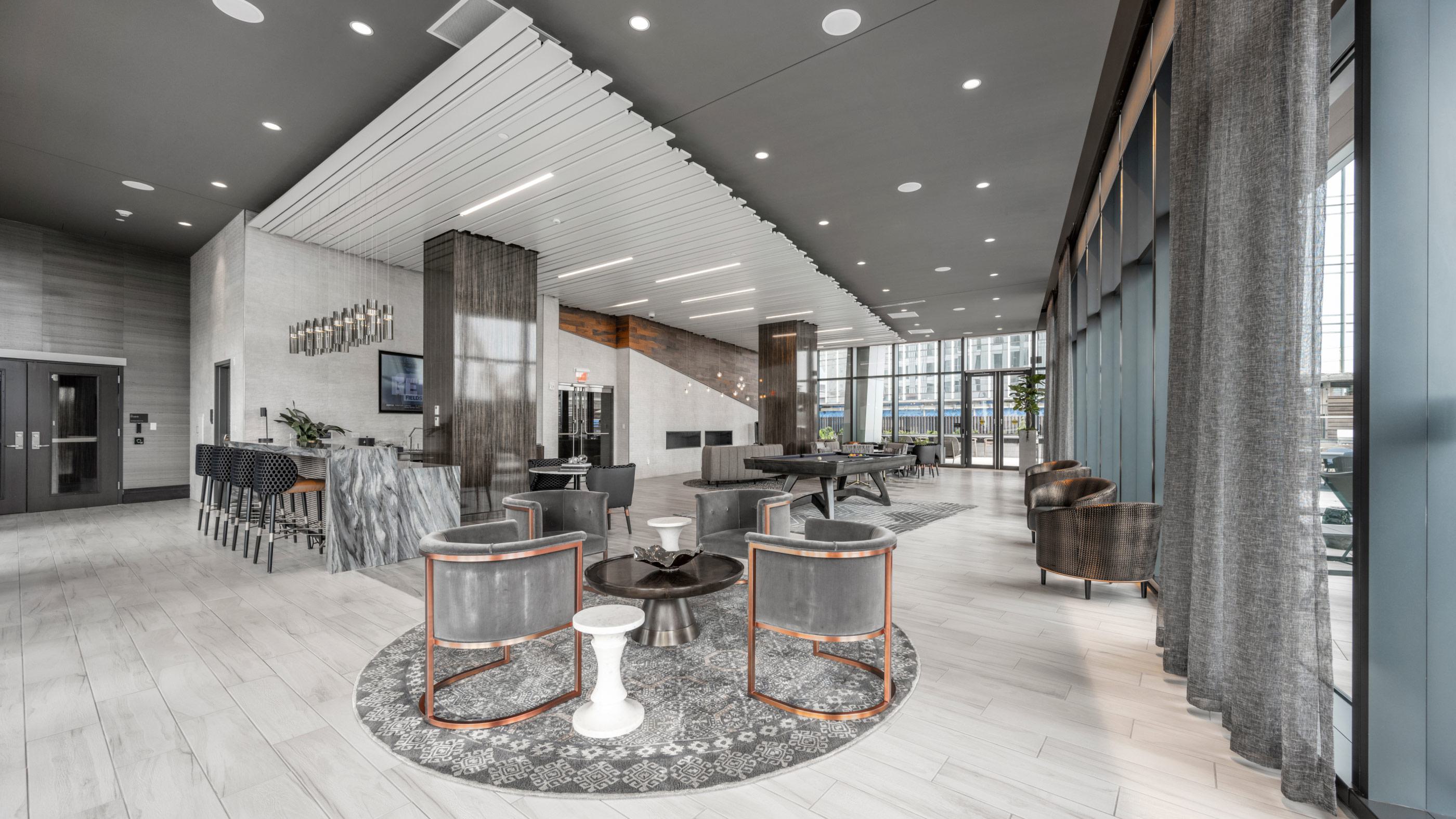 Spacious Sky Lounge at The Sudbury with bar seating, modern decor, multiple lounge areas, and full-height glass walls overlooking the city.