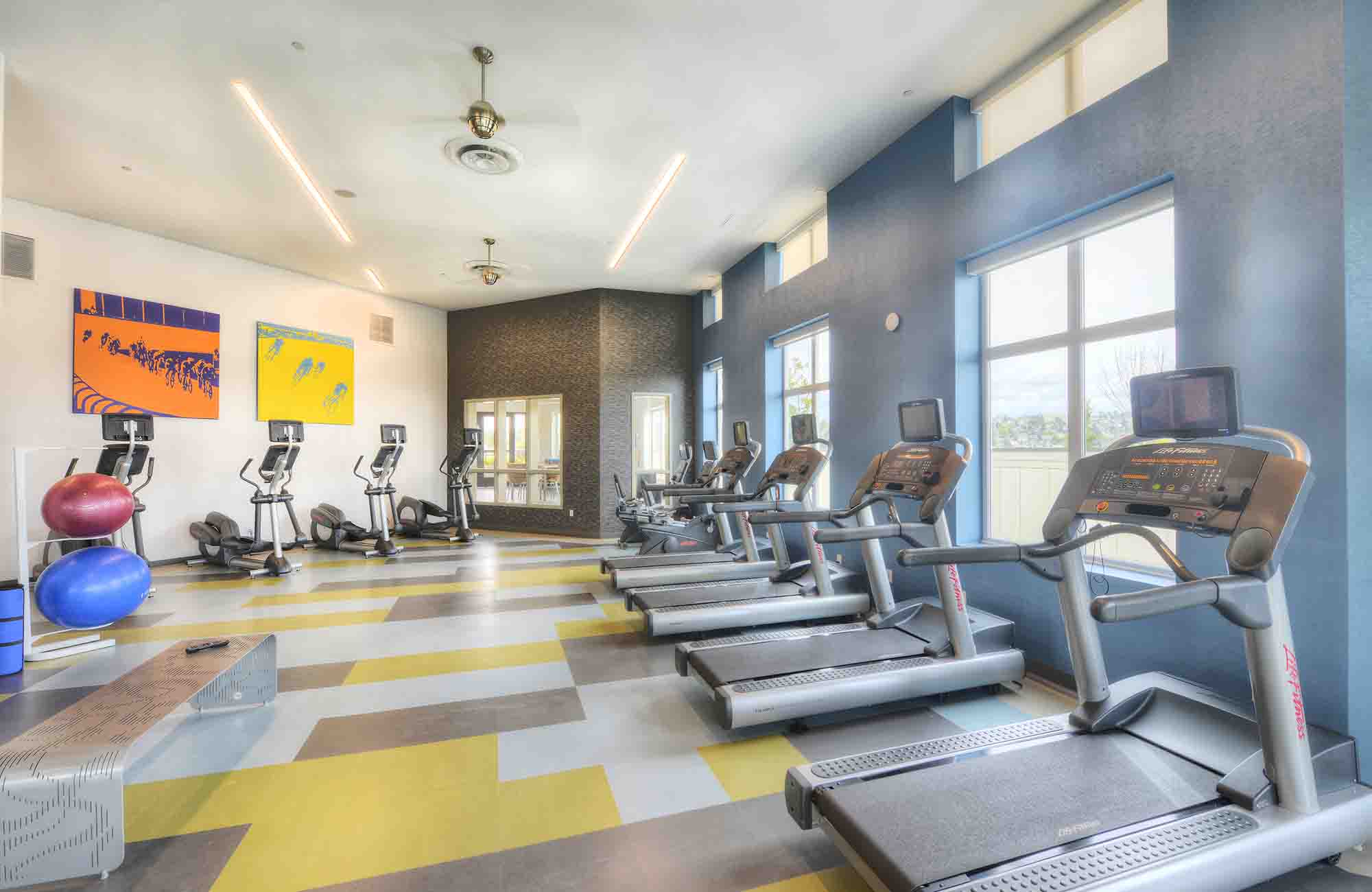 Treadmills in Urbana Apartments’ fitness center positioned along tall windows, with patterned flooring, high ceilings, and natural light filling the room.