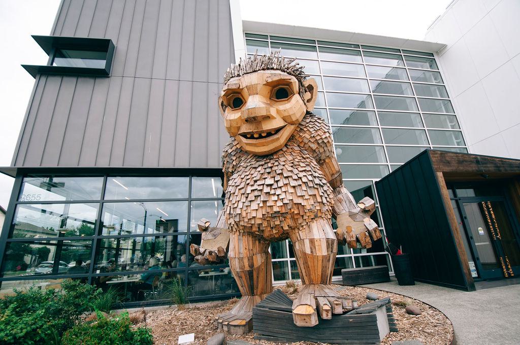 Large wooden troll sculpture outside the National Nordic Museum, built from reclaimed wood with shaggy textures and an expressive face, standing in front of the museum’s glass façade.