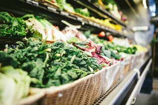 close up of a produce aisle with fresh kale and vegetables in straw baskets