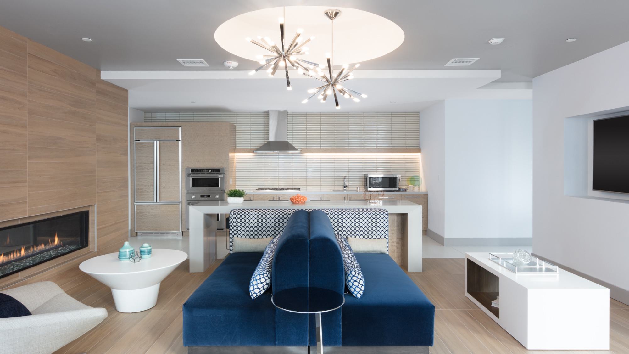 Modern clubhouse lounge at The Triton with a sleek open kitchen, blue velvet seating, linear fireplace, and contemporary lighting.