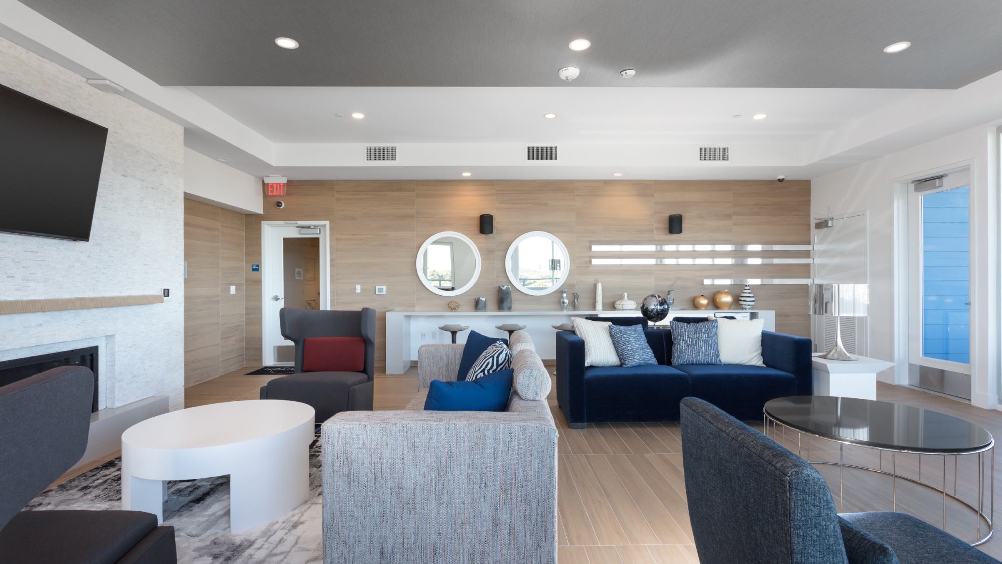 Bright multipurpose lounge at The Triton featuring large windows, layered seating, circular mirrors, and modern décor.