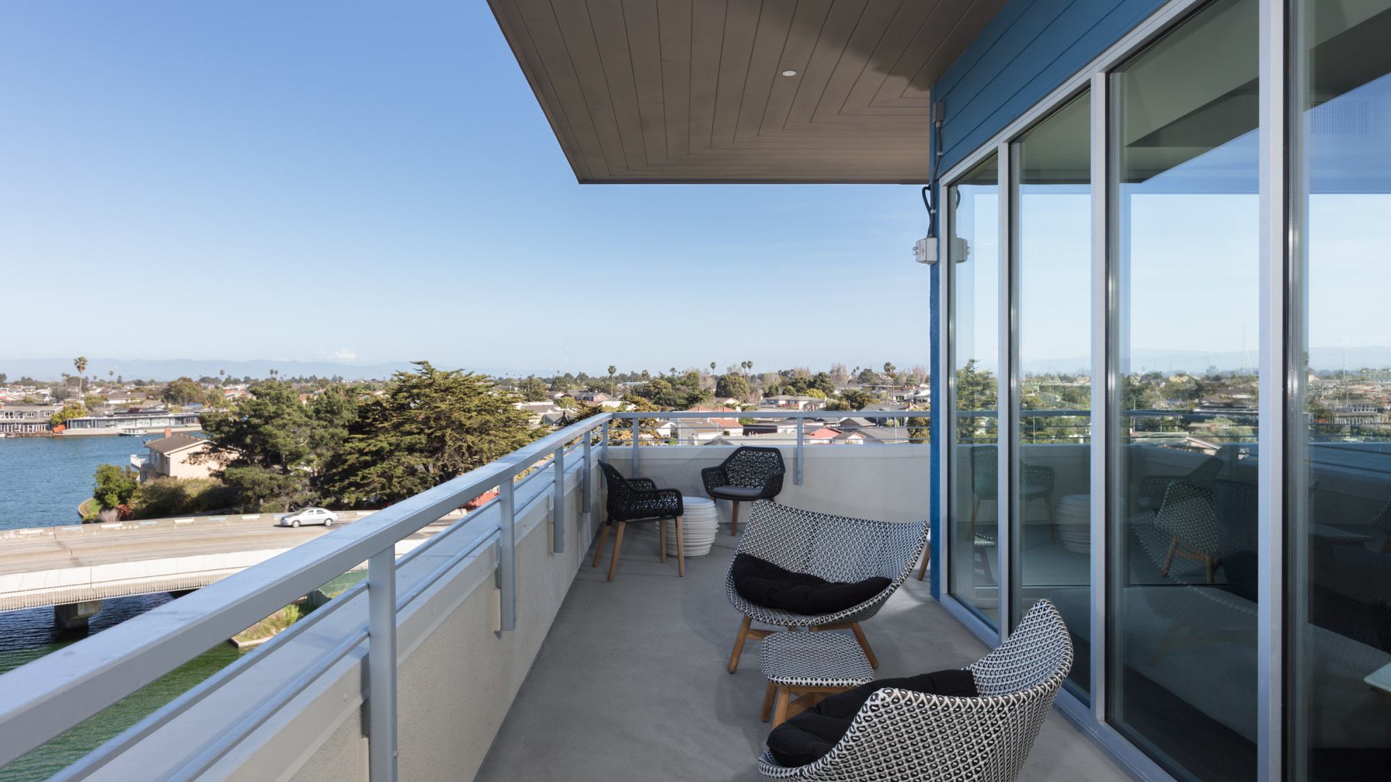 Private lounge balcony at The Triton with woven lounge chairs, railing views of Foster City’s lagoon, and a shaded overhang.