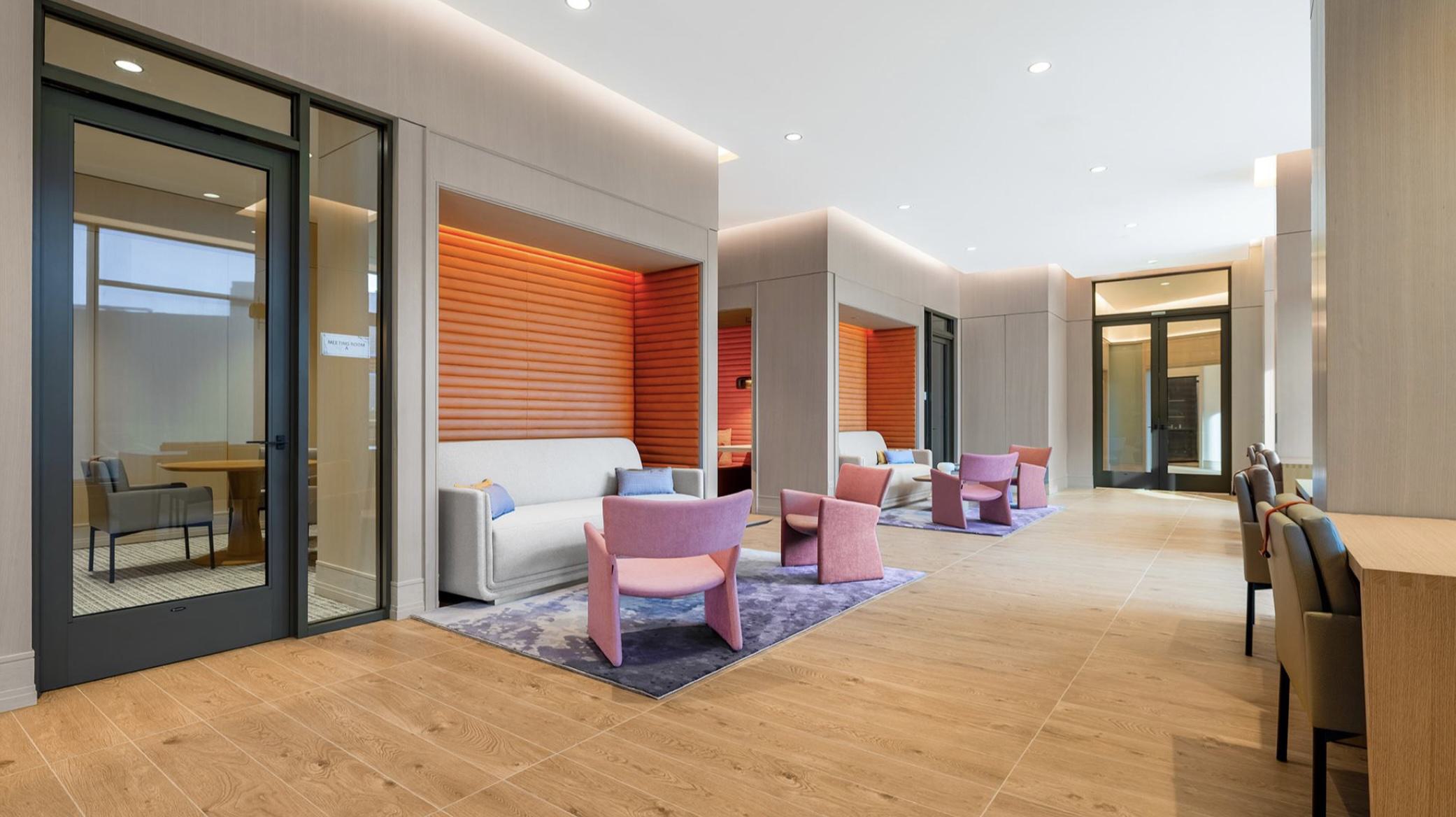 Private glass-door conference rooms at Aerie’s coworking lounge, shown with modern tables, upholstered chairs, and bright natural light filtering in from the larger workspace.