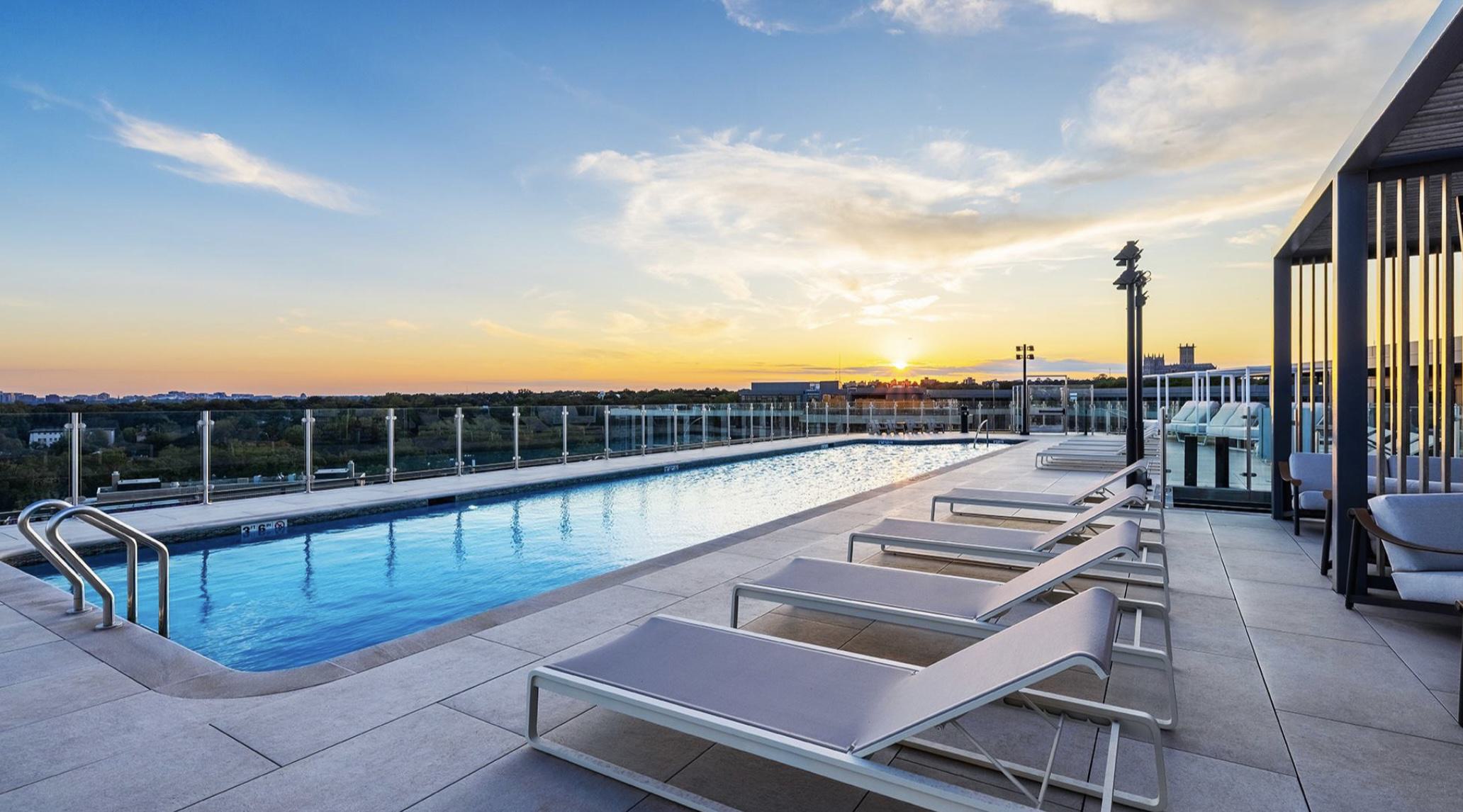 Rooftop pool deck at Aerie showing glass railings, modern loungers, slatted cabanas, and a wide view over the tree canopy and DC skyline.