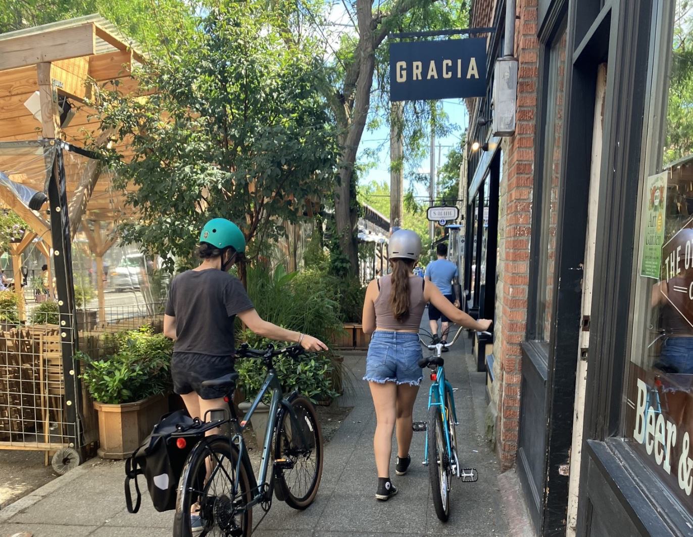 bikers walking their bikes along a charming sidewalk near storefronts in ballard