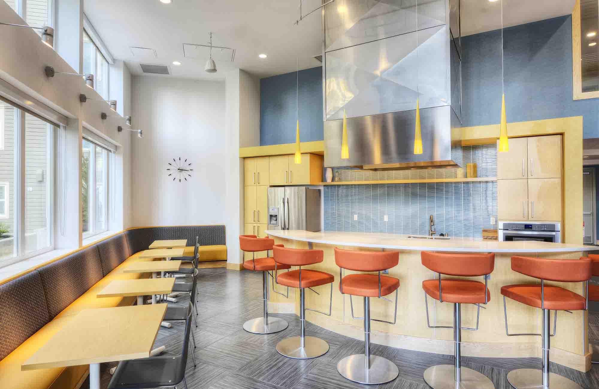  lounge area featuring a built-in banquette with café tables, a kitchenette with wood cabinetry and bar seating, and warm pendant lighting.