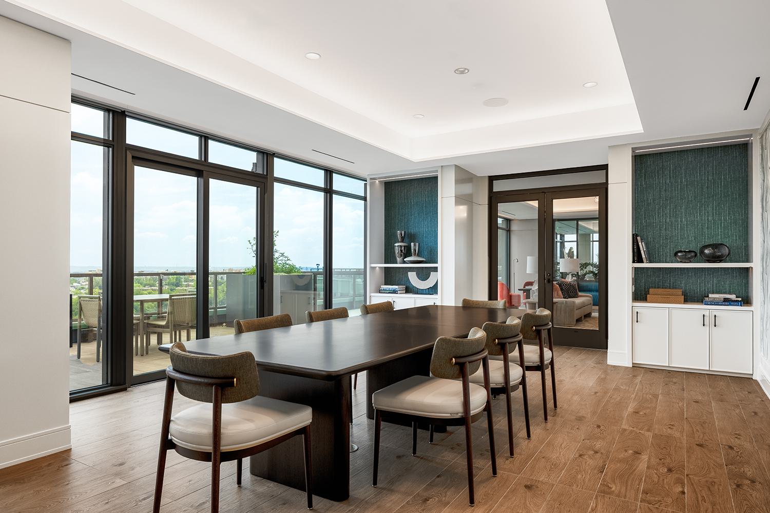 Private dining room at Aerie featuring a long dark-wood table, upholstered chairs, built-in shelving niches, and floor-to-ceiling glass doors opening to the terrace with views over DC.