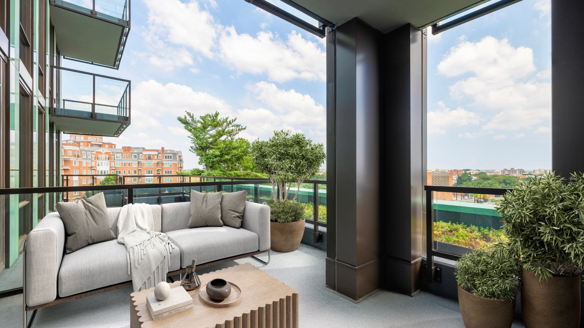 Private balcony at Aerie with a light gray outdoor sofa, potted greenery, and views of surrounding historic buildings and treetops in Woodley Park.
