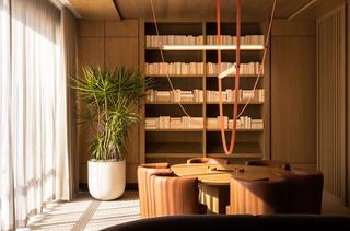 Oak-wrapped library and meeting room with neutral bookshelves, round table, leather chairs, sculptural ceiling light, and soft natural light.